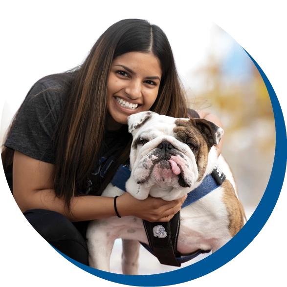 A woman smiling with an English Bulldog in an outdoor setting.