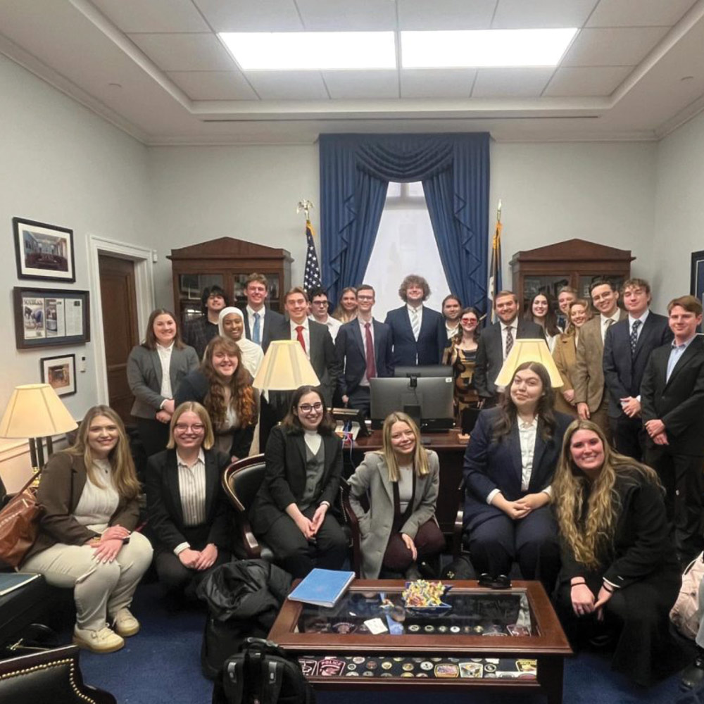 A group of twenty-four people in business attire in a formal office setting.