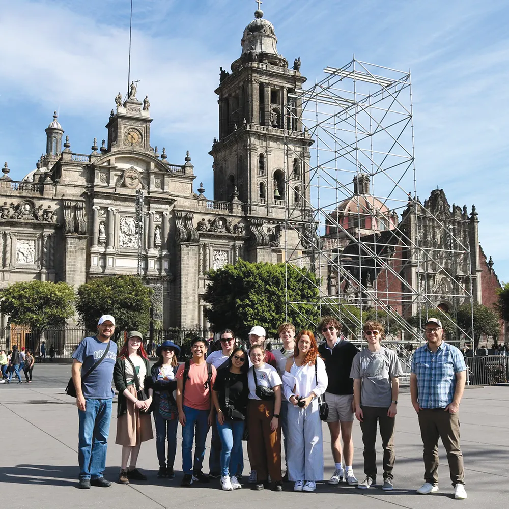 Group of people in front of the Metropolitan Cathedral in Mexico City with scaffolding beside the structure.
