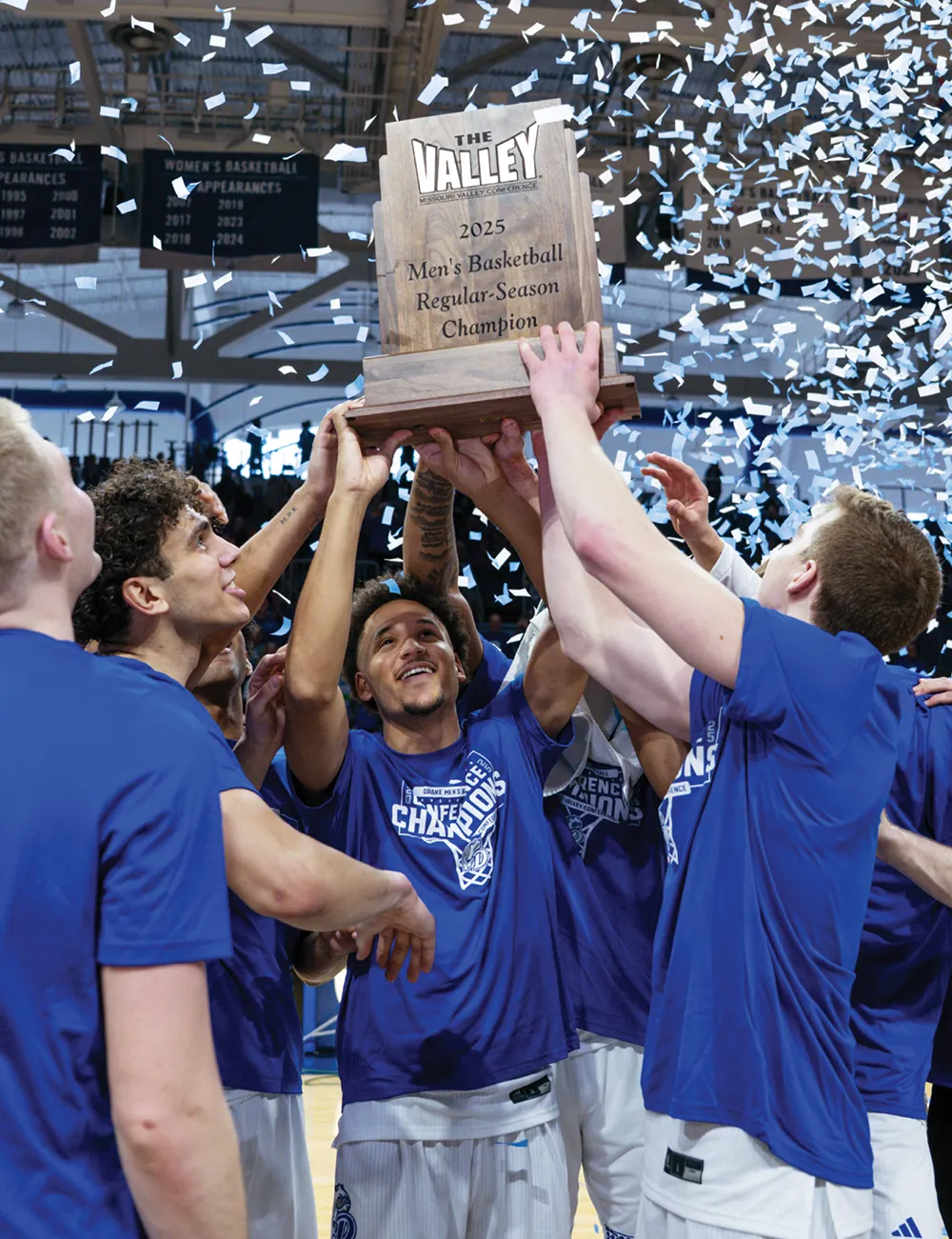 Basketball players celebrate, holding a trophy with confetti falling around them.
