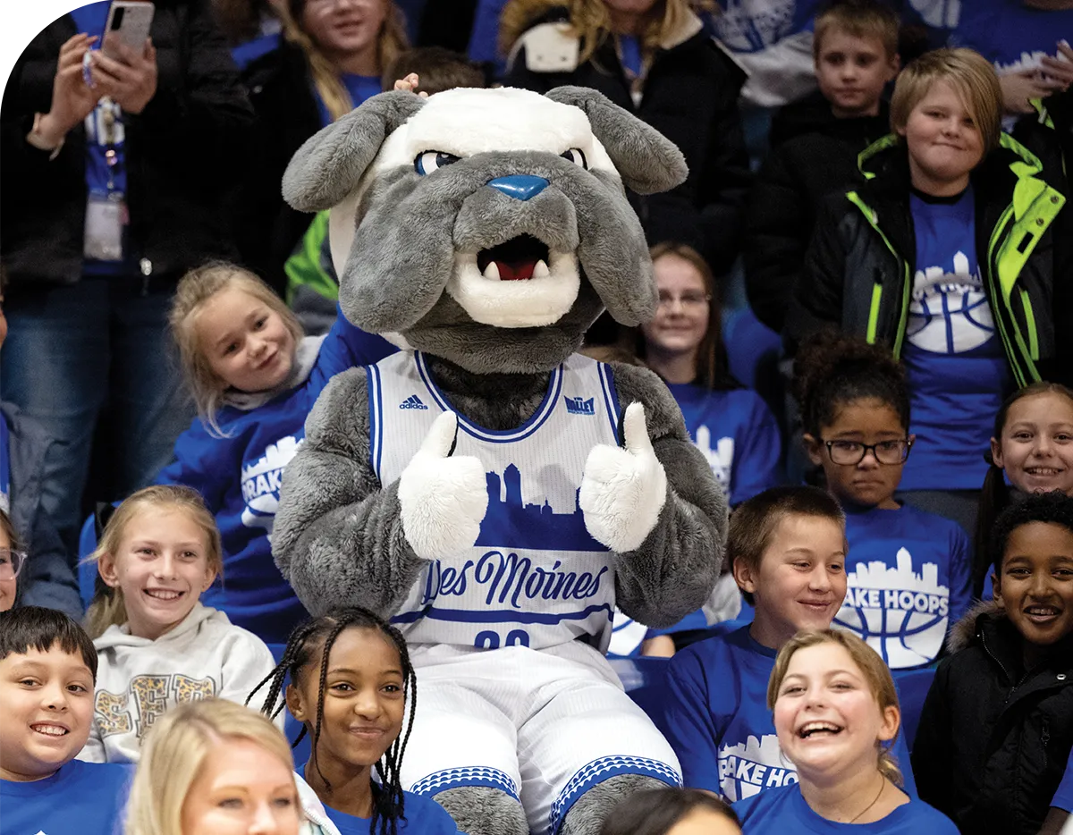 A bulldog mascot in a basketball jersey sits among smiling children.