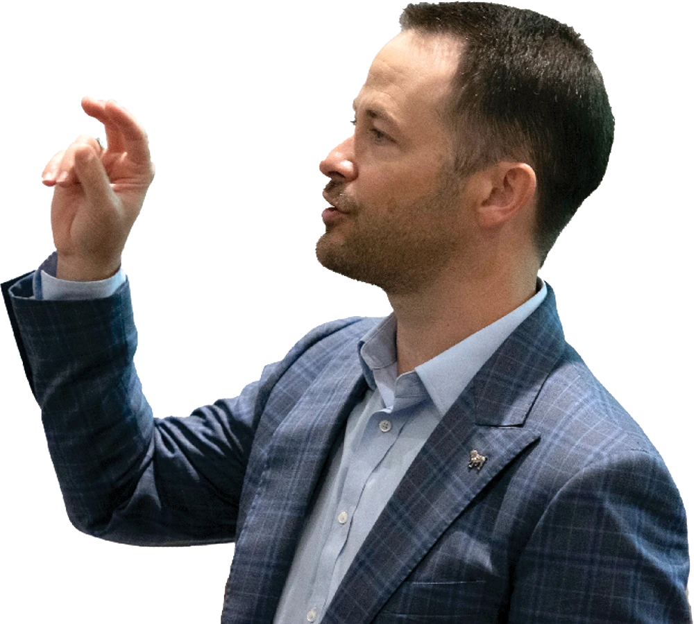 Man in a blue checked suit gesturing with a raised hand.