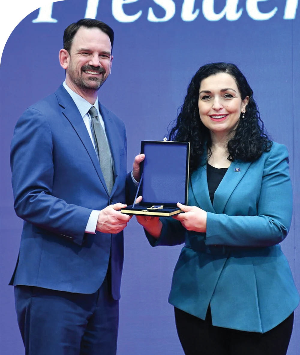 Two people in blue blazers holding an open black case against a blue backdrop.