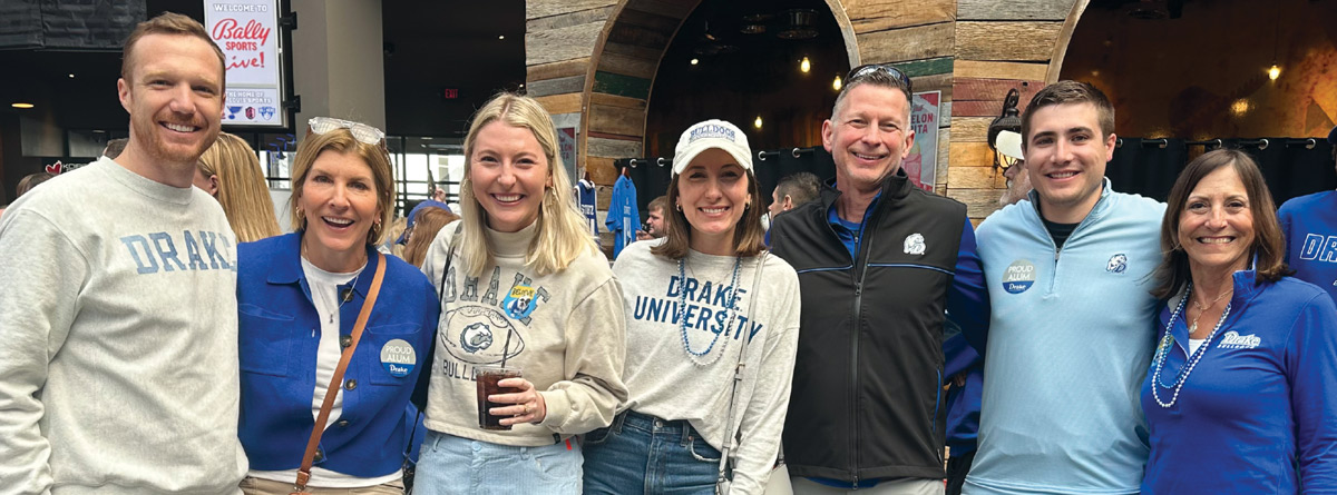A group of people wearing Drake University apparel, smiling inside a venue.