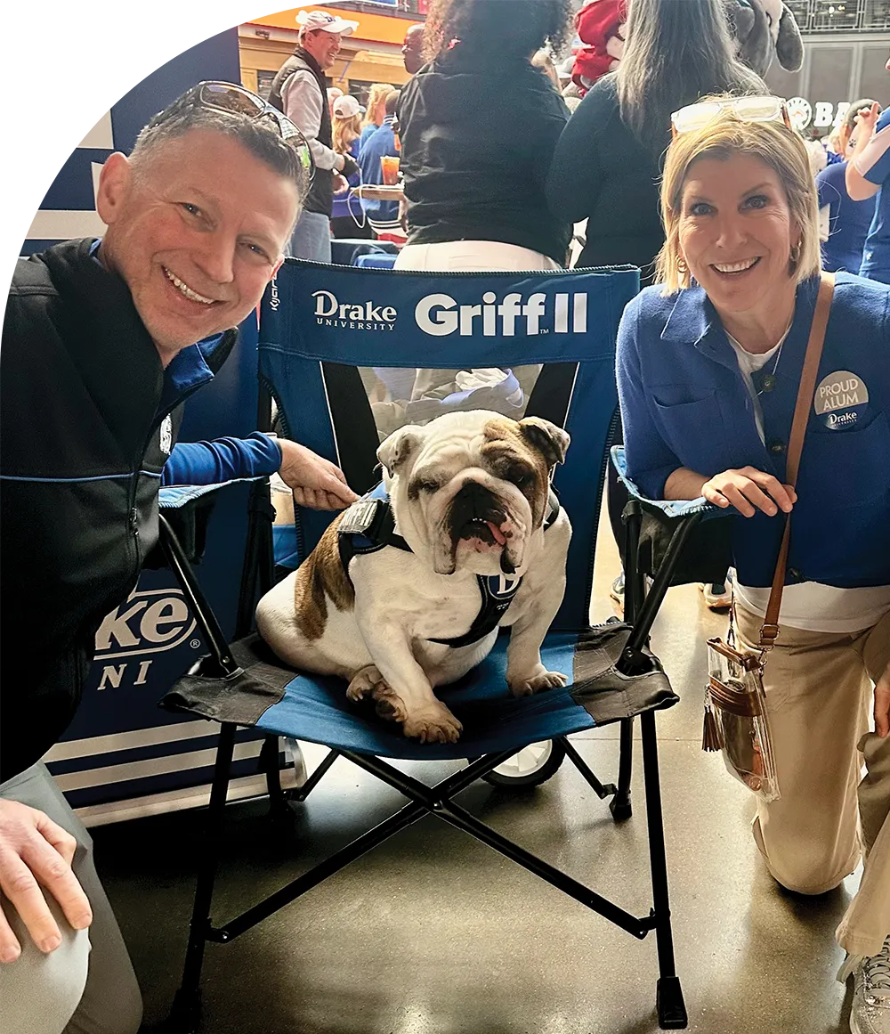 A bulldog named Griff II sitting on a chair with two people crouching beside it, smiling.