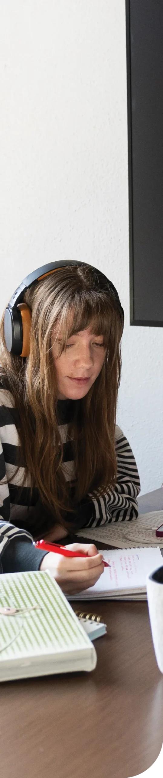 Person wearing headphones, writing at a desk with a notebook.