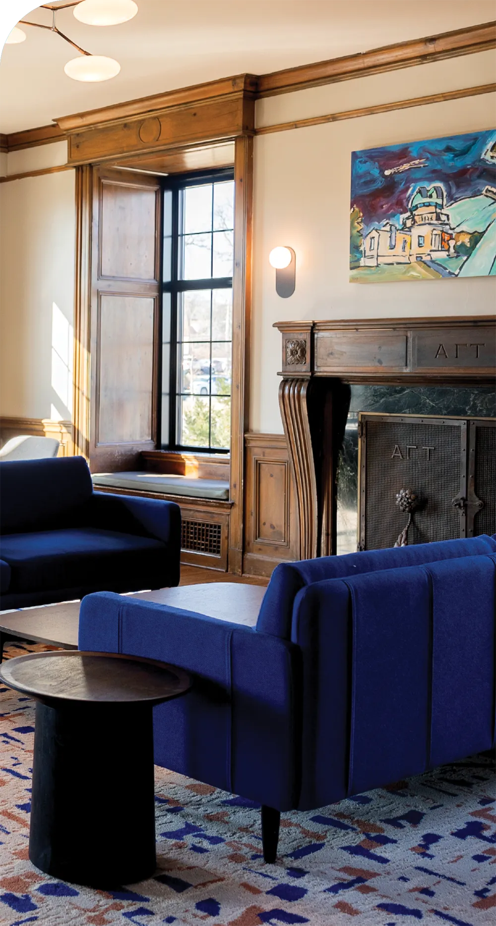 Living room with blue armchairs, wooden fireplace, and abstract painting above.