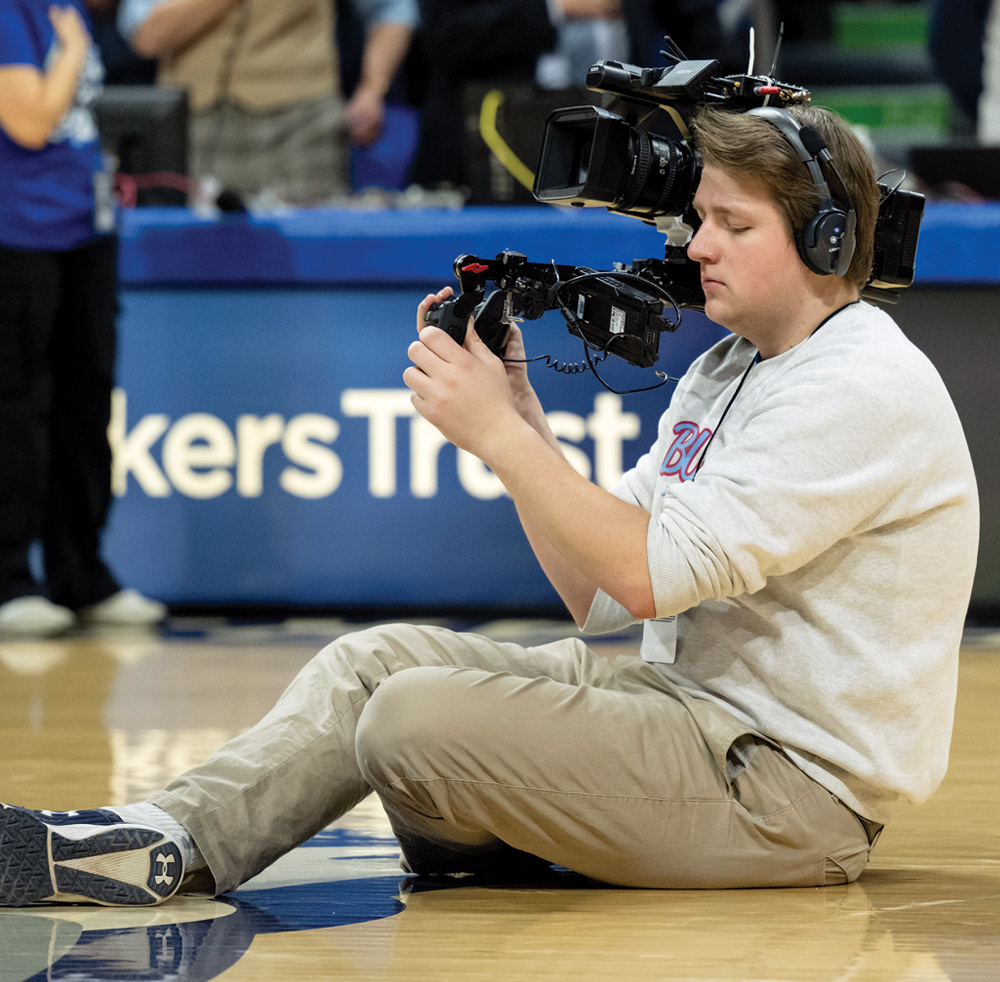 Person on a basketball court operating a large video camera.