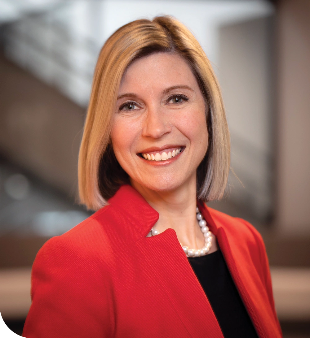 Person smiling in a red blazer with a pearl necklace.