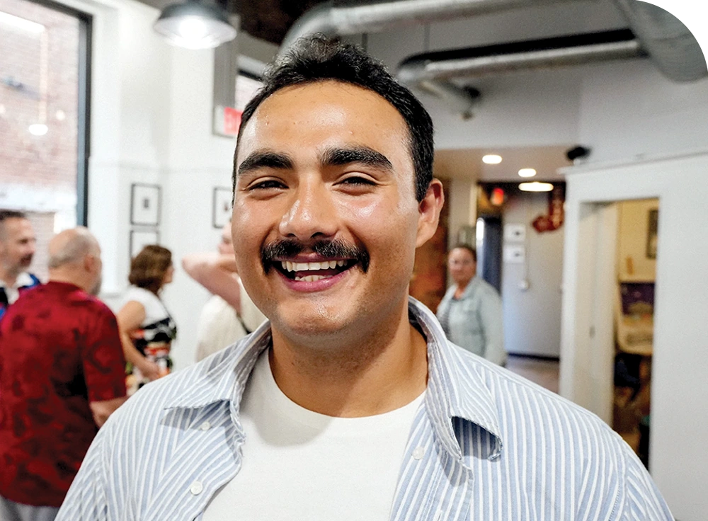 Smiling man with a mustache in a social gathering setting indoors.