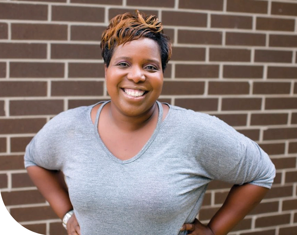 Person smiling in front of a brown brick wall.