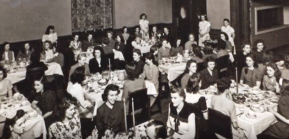 Black-and-white photo of women seated at dining tables in a hall.