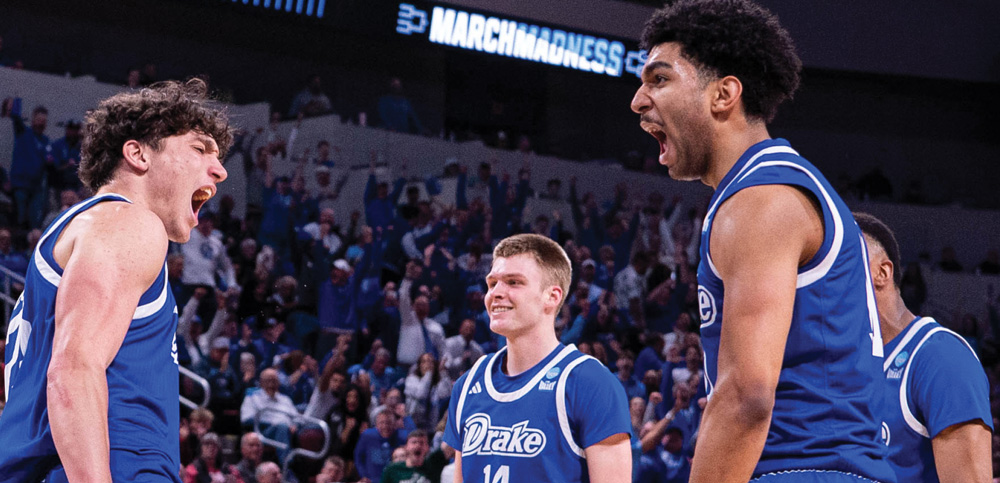 Four basketball players in blue jerseys express excitement and intensity on the court.