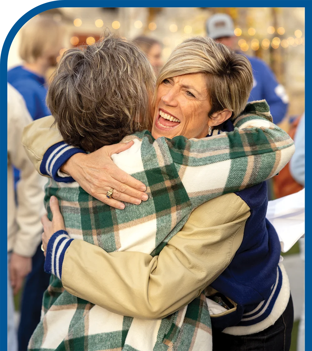Two women embracing at an outdoor event with lights in the background.