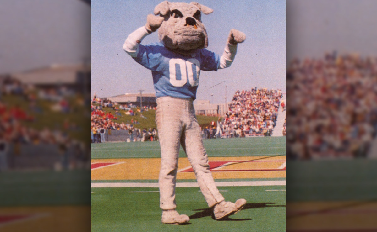 Person in a bulldog mascot costume with a blue jersey numbered "00" on a football field.