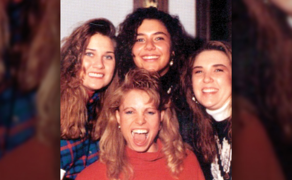 Four women smiling closely together indoors.