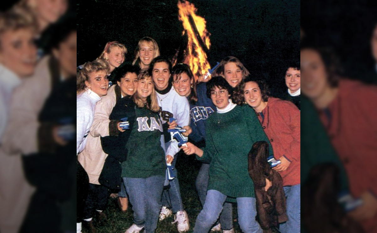 A group of people smiling in front of a nighttime bonfire.