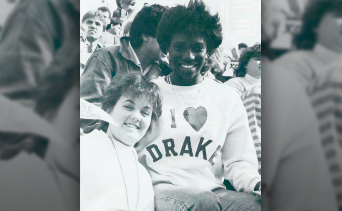 Two people smiling and posing for a photograph in a crowd, one wearing a sweatshirt that reads I HEART DRAKE.