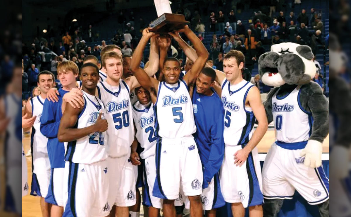 A basketball team and a mascot celebrate on the court with a trophy.