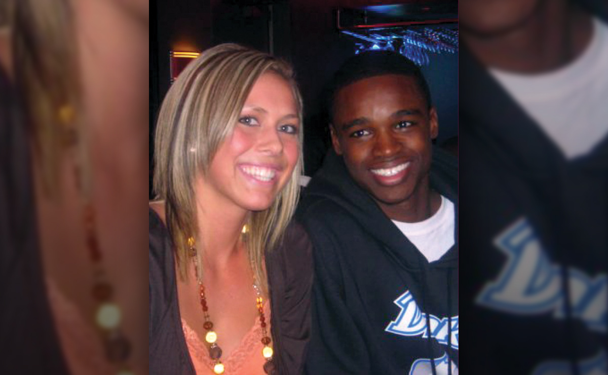 Two people smiling, sitting side by side in a dimly lit room.