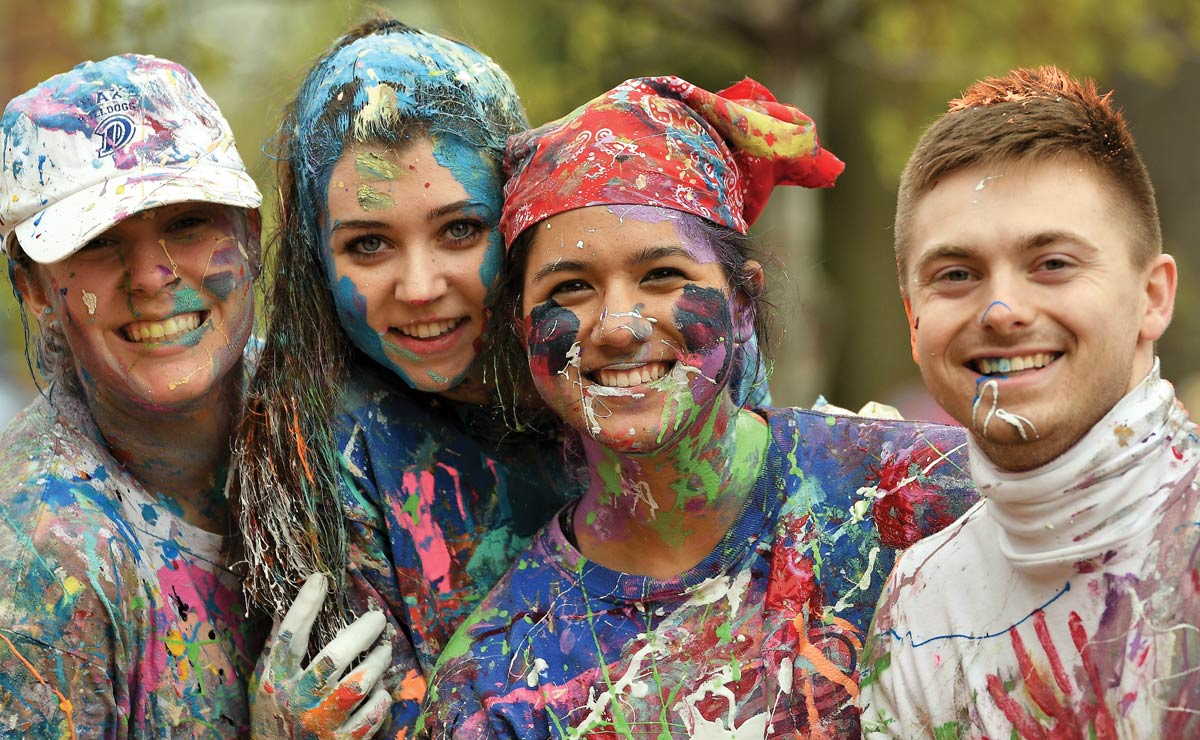 Four people smiling, covered in colorful paint splashes.