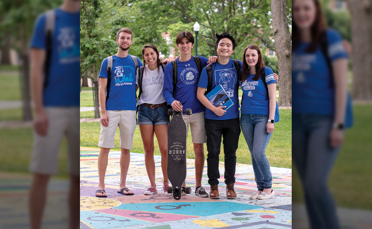 Group of five students standing on colorful pavement outdoors, smiling.