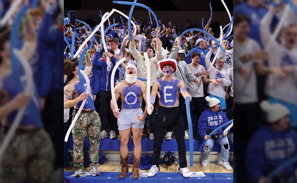 Enthusiastic crowd of students at a sporting event, including three shirtless males painted blue on their chests.