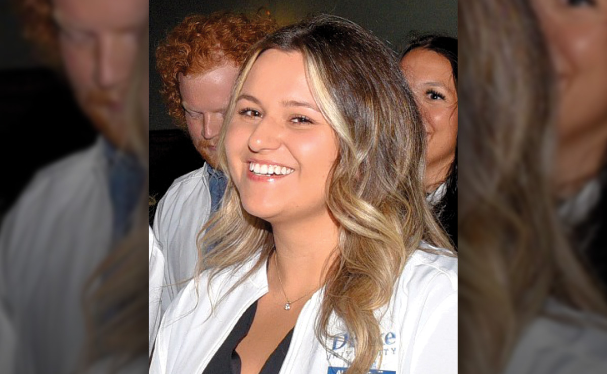 A smiling woman with long, highlighted hair wearing a white coat.