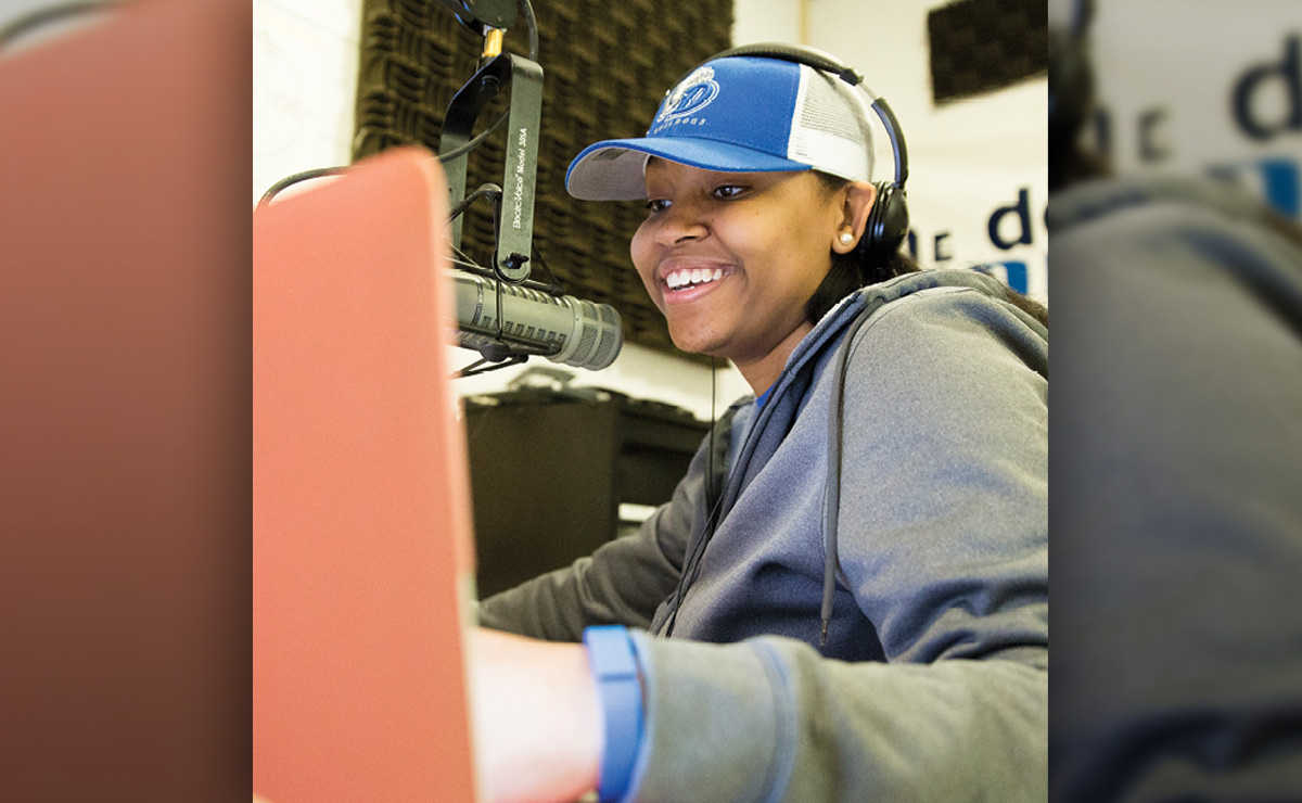 Person smiling at a microphone in a recording studio.