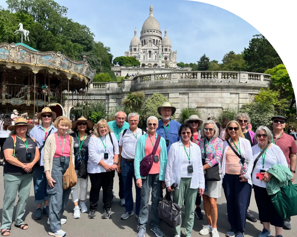 A group portrait of senior travelers from a university lifelong learning program enjoying a guided tour in front of a historic white stone basilica in France.