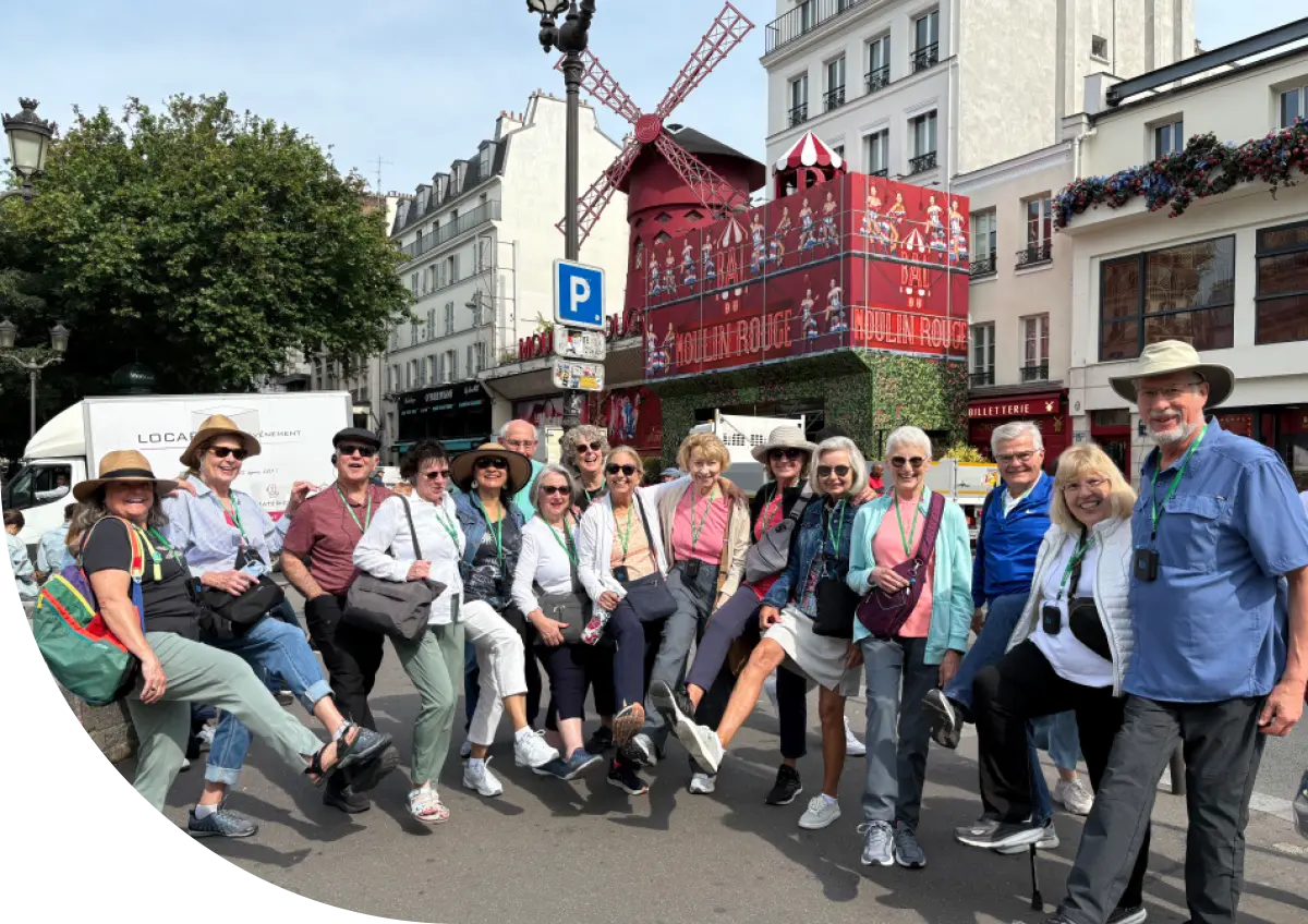 OLLI at Drake University travel group posing with a 'can-can' leg kick in front of the iconic red windmill of the Moulin Rouge in Paris.