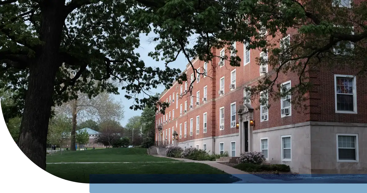 Exterior view of a multi-story red brick dormitory building at Drake University, surrounded by green lawns and mature shade trees.