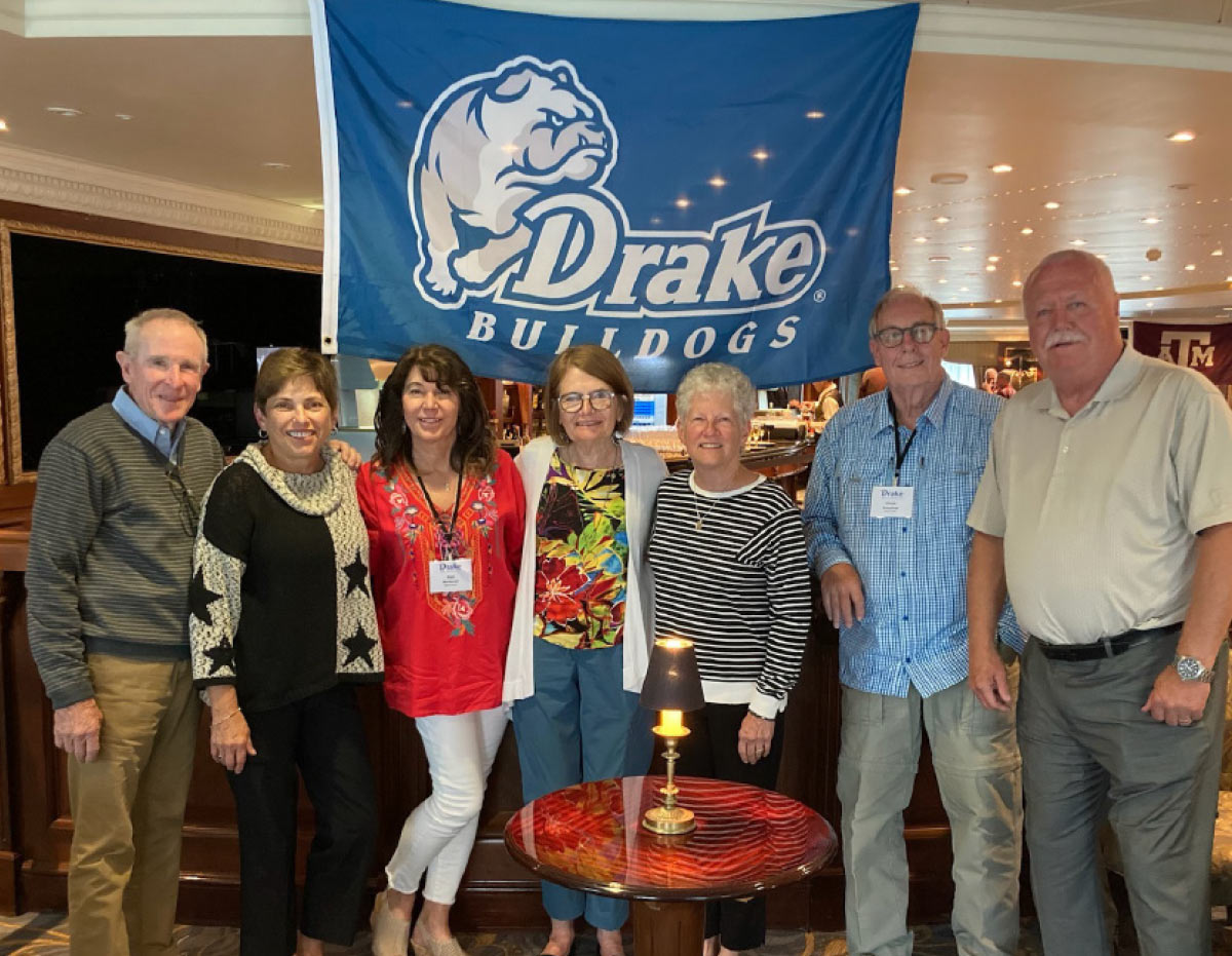 Seven people posing together in a bar or restaurant in front of a blue "Drake Bulldogs" flag.