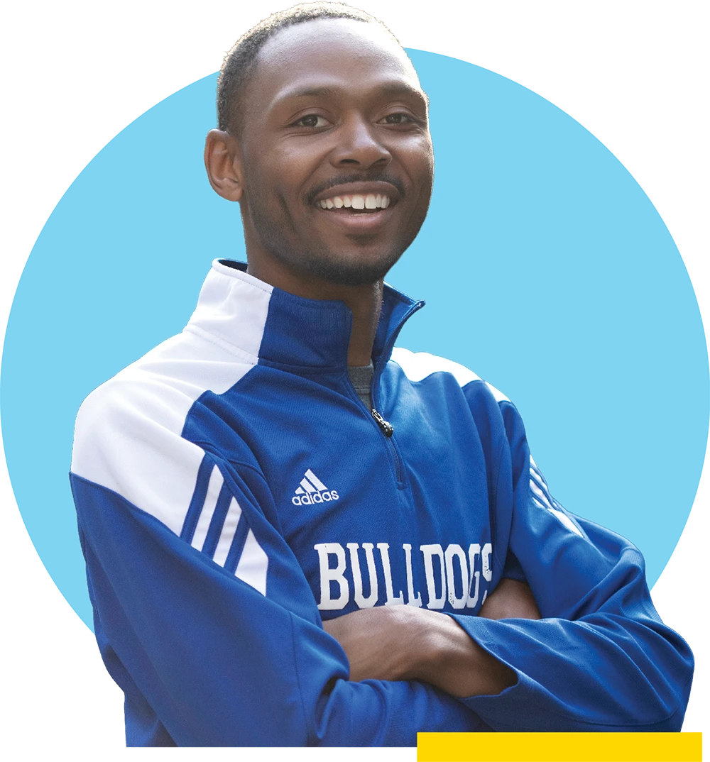 Donovan McCamey wears a blue and white "Bulldogs" Adidas athletic jacket with his arms crossed against a light blue circular background.