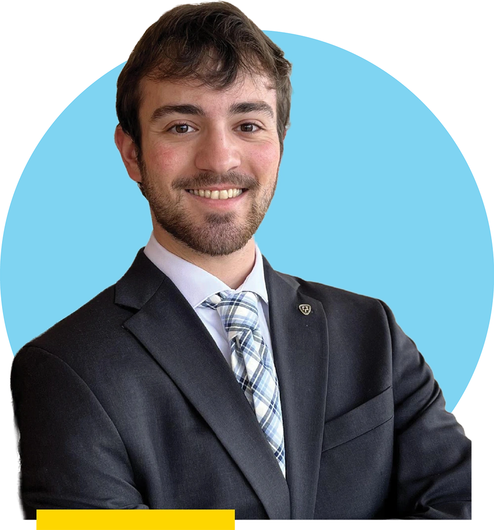 Trevor Stevens wearing a dark suit, light-colored shirt, and plaid tie against a light blue circular background.