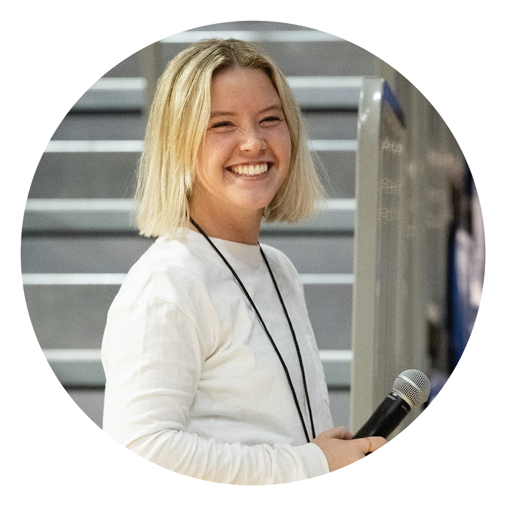 Mel Dygert smiling, holding a microphone at an event.