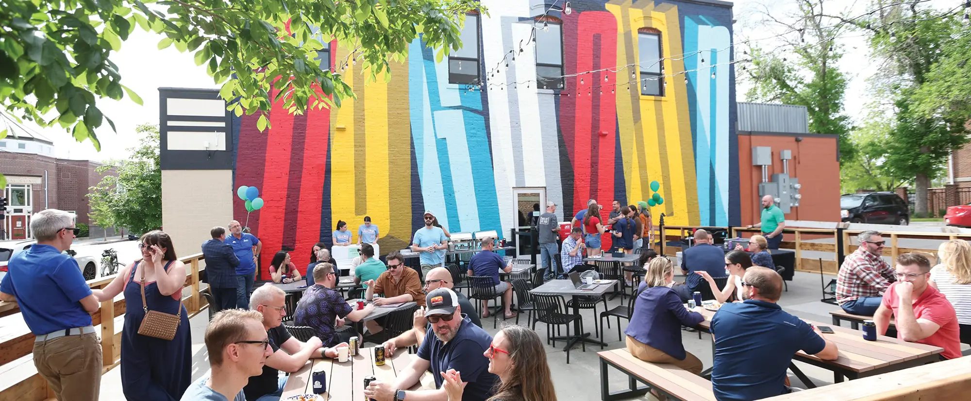 A wide shot of the vibrant, multi-colored "Dogtown" mural with people enjoying the outdoor patio space in front of it.