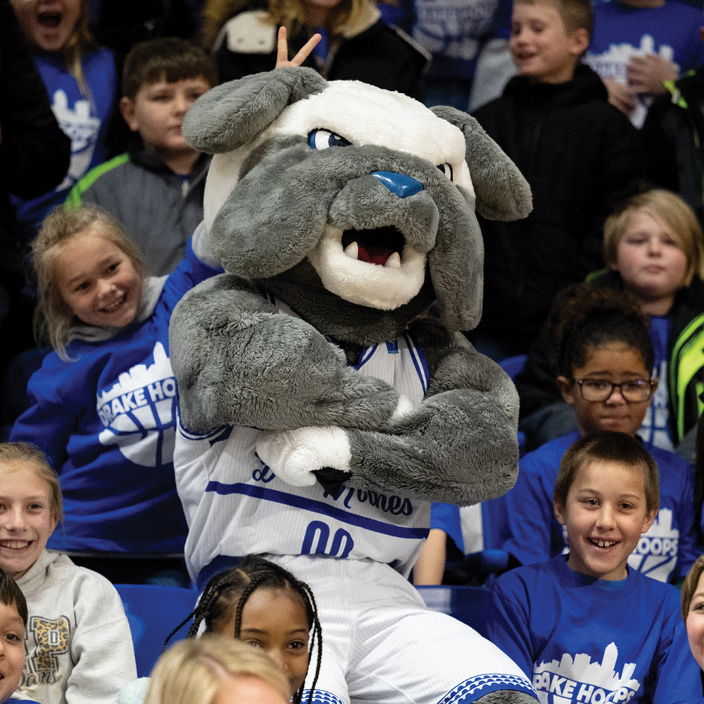 A close-up of the Drake University Bulldog mascot (Griff) interacting with young fans, highlighting the family-friendly "Drake Hoops" culture.