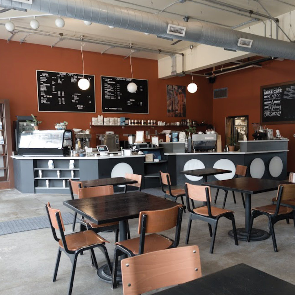 The interior of the neighborhood coffee shop, showing the menu boards, coffee counter, and seating area where students and locals gather.