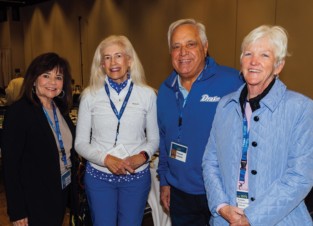 Four Drake University alumni, two men and two women, stand together smiling. They wear "Drake Alumni" lanyards and name tags, including one for Frank Ursini.