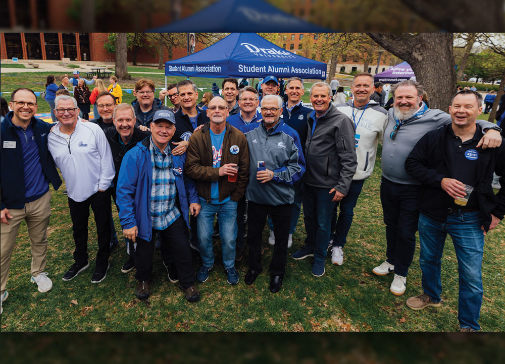 A large group of men in casual Drake University and Sigma Chi apparel pose together on a lawn. A blue "Student Alumni Association" tent is visible in the background behind them.