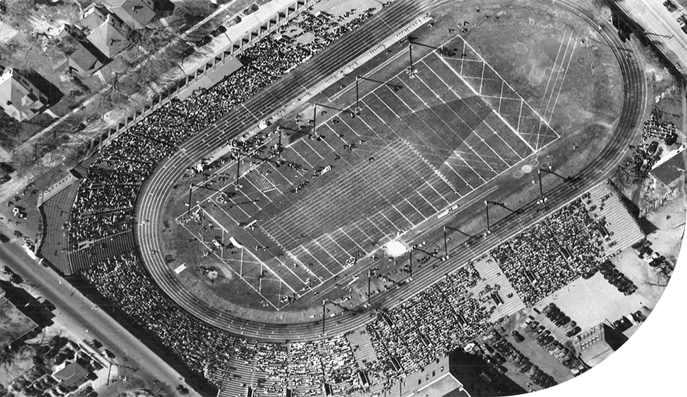 Black and white aerial view of a packed stadium during a track and field event, showing the oval track, infield, and crowds filling the horseshoe-shaped stands.