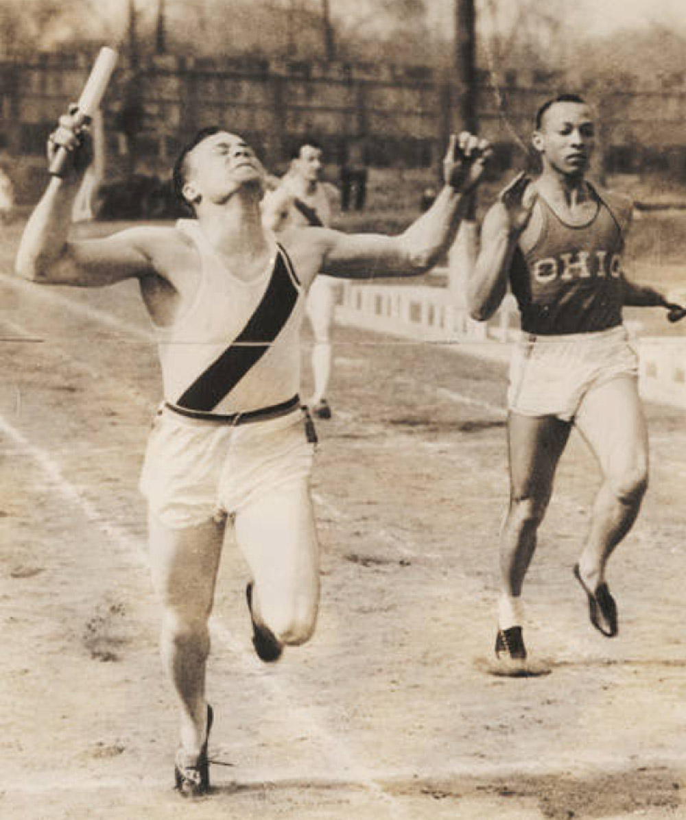 Vintage sepia photo of a relay runner crossing the finish line with arms raised and baton in hand, narrowly leading a competitor wearing an "OHIO" jersey.