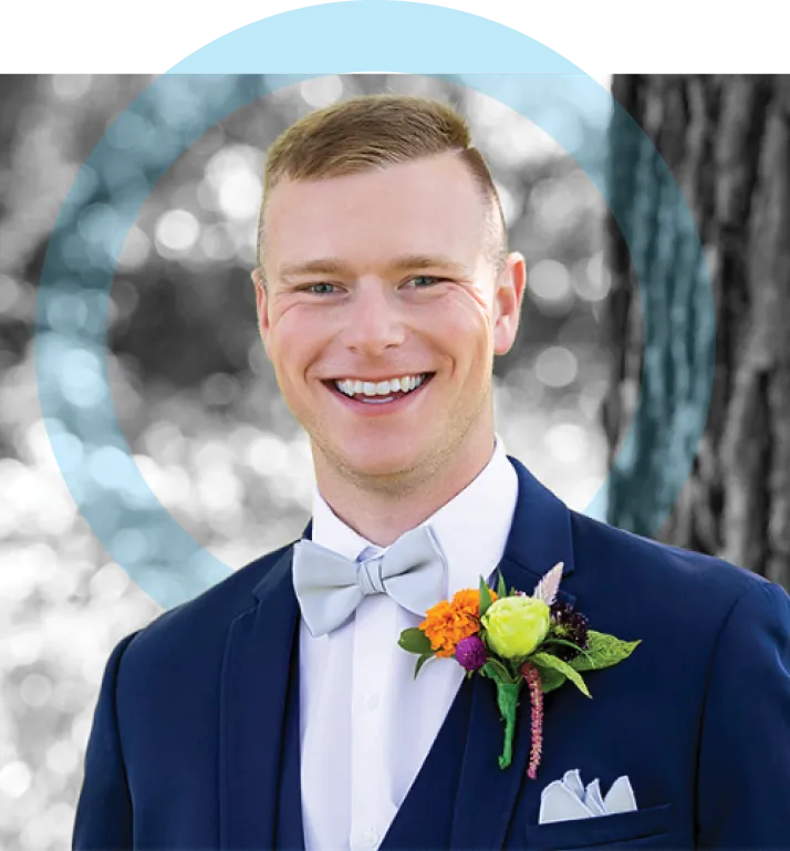 Formal portrait of an adult man wearing a navy suit, white shirt, and bow tie with a boutonniere, smiling outdoors with trees softly blurred in the background and a circular graphic element overlaid.