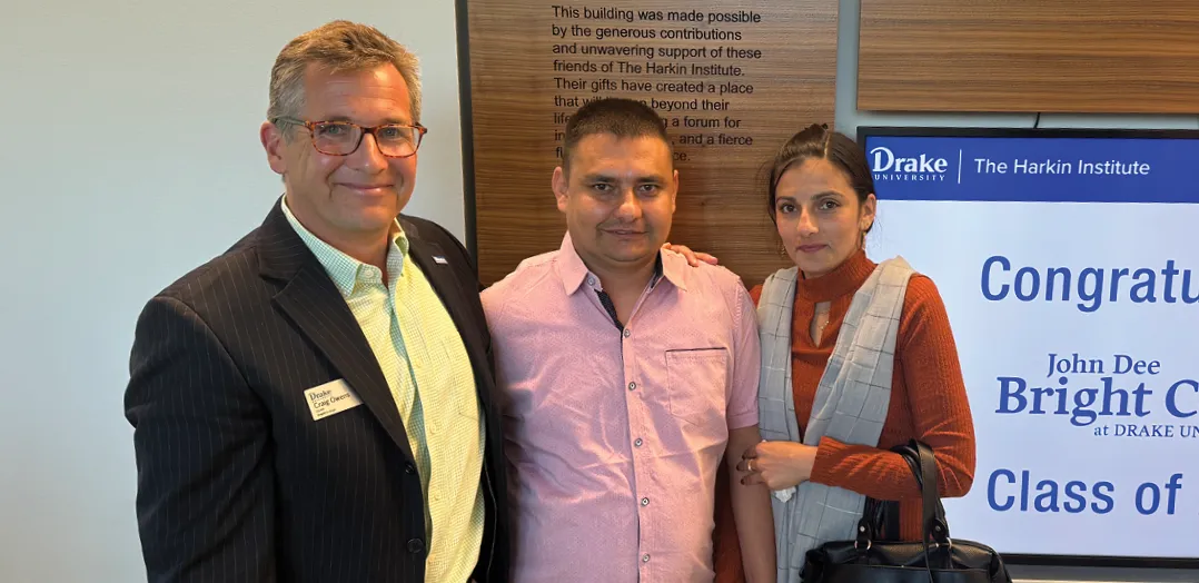 A formally dressed man and woman pose together indoors in front of a mural featuring historical imagery, smiling toward the camera during an official or ceremonial event.
