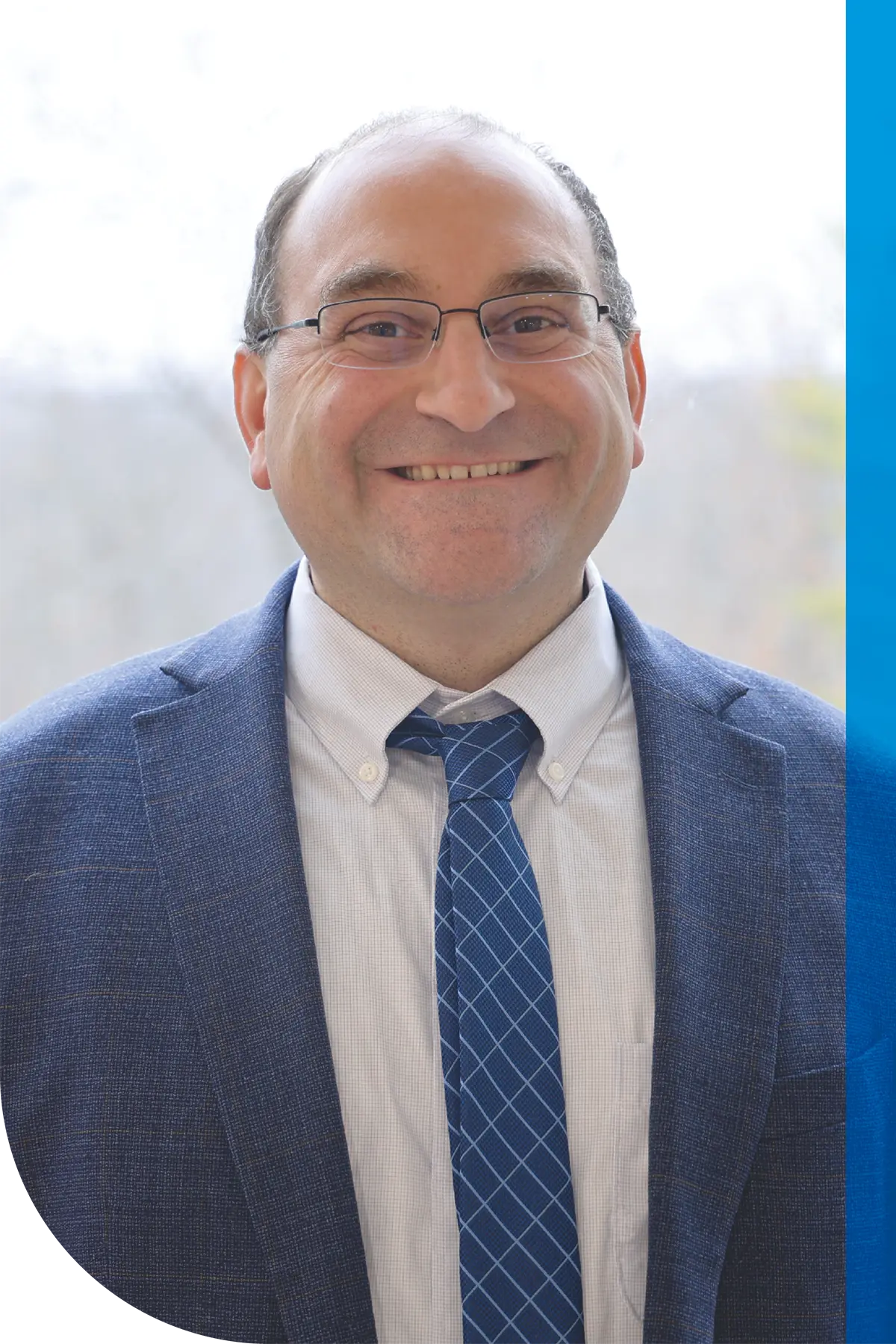 Close-up portrait of Joseph M. Valenzano III wearing glasses, a blue patterned tie, and a blue suit jacket.
