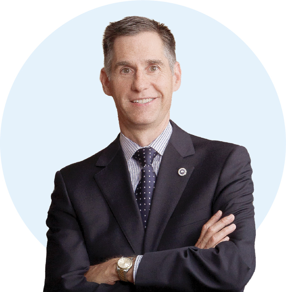 Studio portrait of John P. Smith with short brown hair in a dark suit jacket, polka dot tie, and collared shirt with arms crossed.