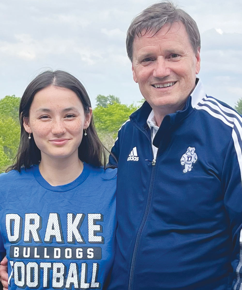 A young woman in a Drake Bulldogs shirt poses outdoors with a man wearing a blue Drake University track jacket.