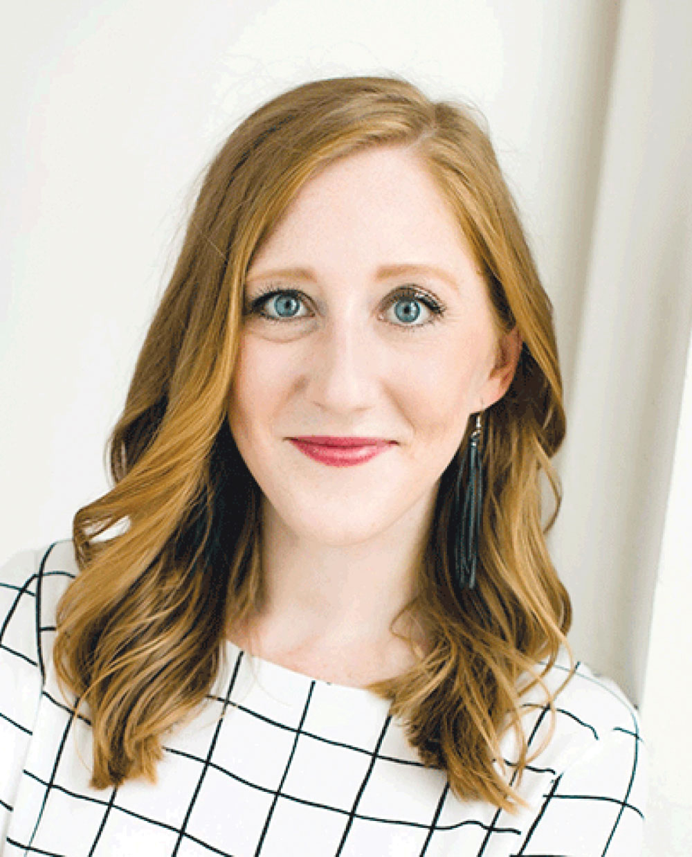 Emilee A. Richardson with long strawberry blond hair wears a white and black grid-patterned top and black earrings.