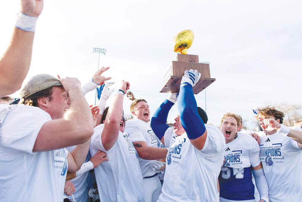 Football players celebrate holding up a gold trophy while wearing Pioneer Football League Champions shirts.